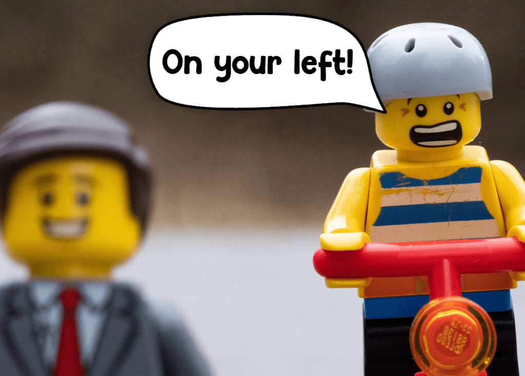 Two Lego figures, one with a helmet riding a scooter saying: "On your left!"